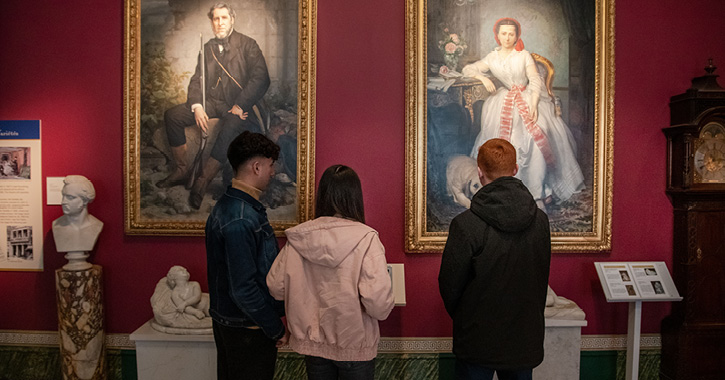 group of three people stood in front of paintings of John and Josephine at The Bowes Museum